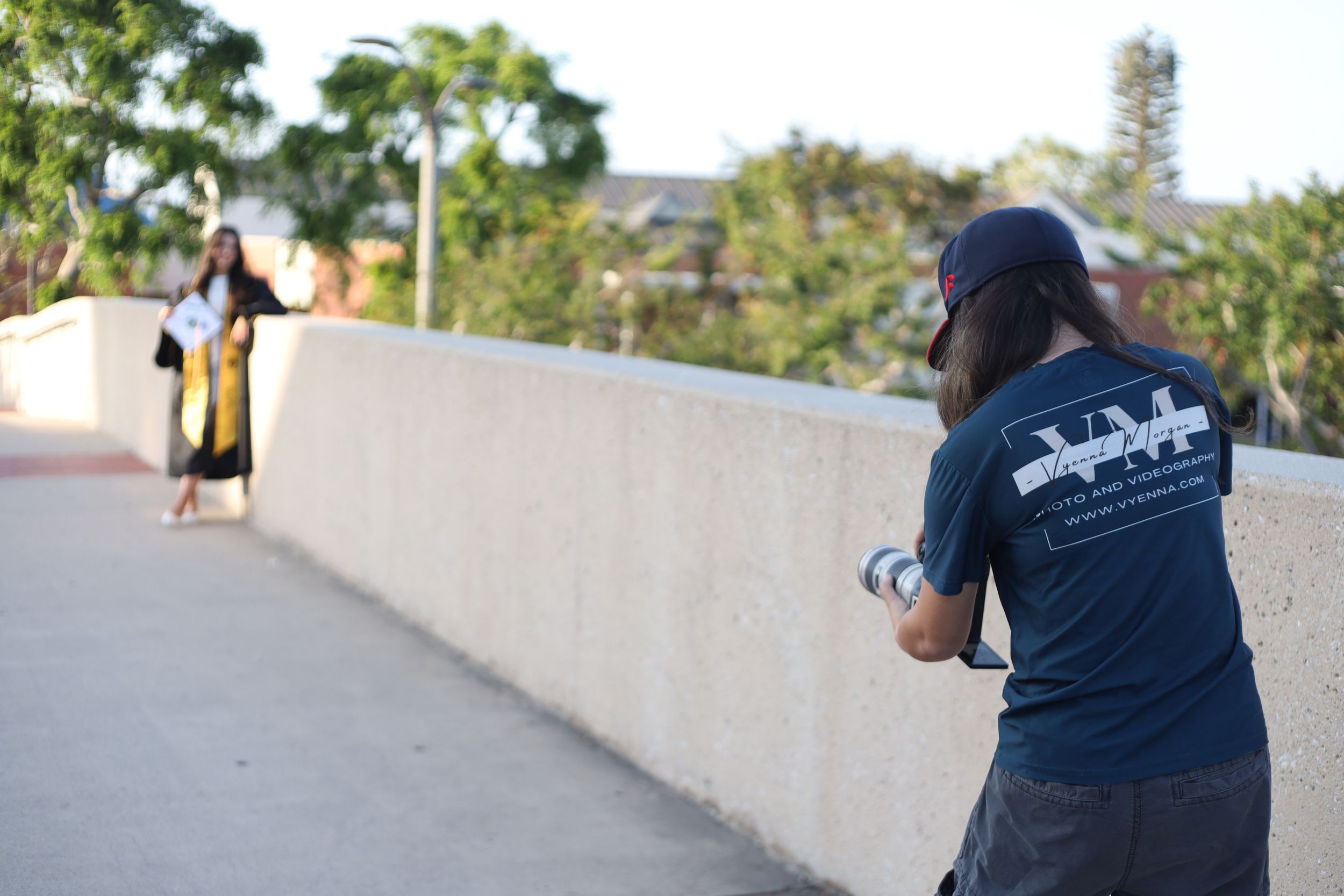 A photographer captures a skateboarder riding along a curved concrete wall on a sunny day.