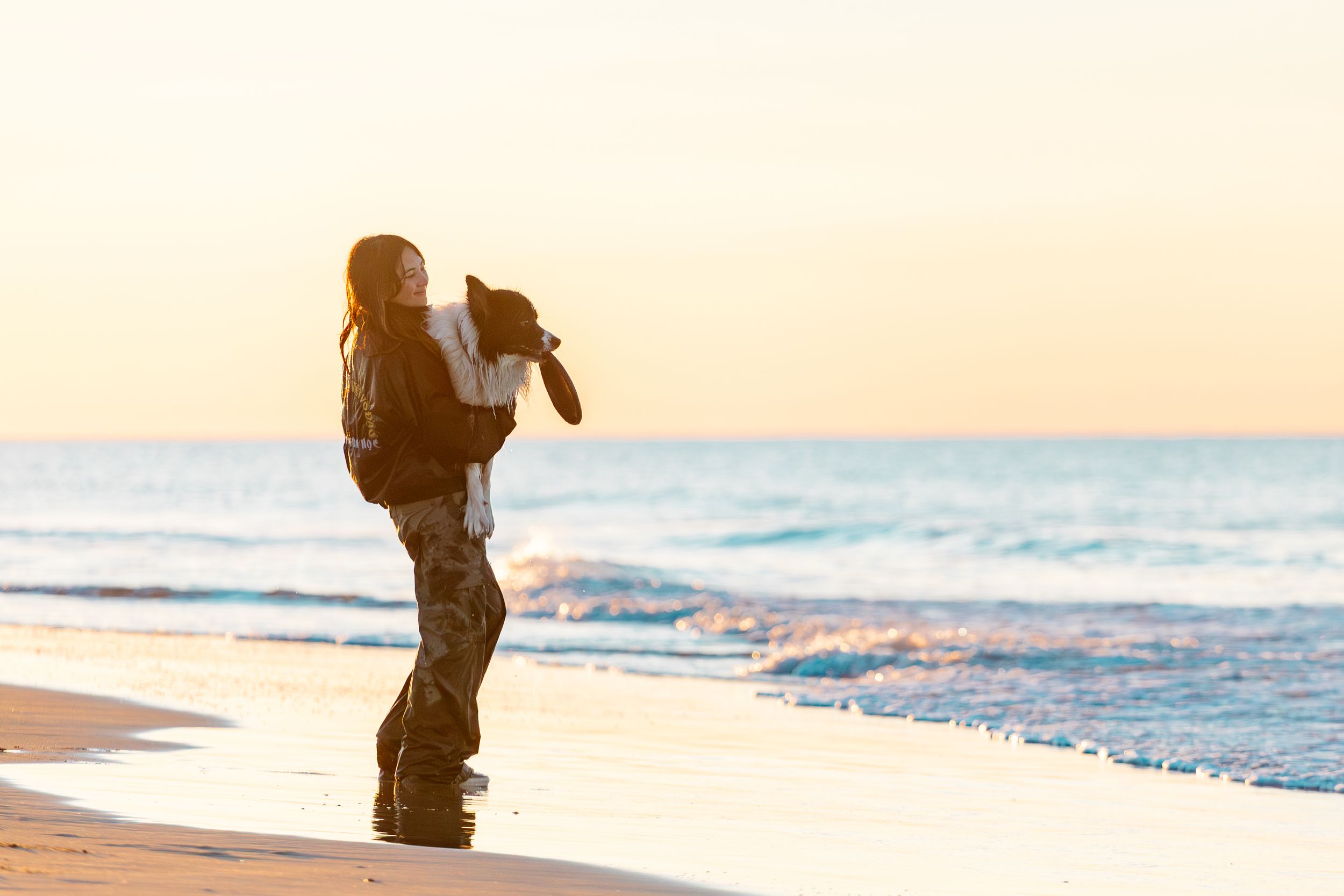 Silhouette of someone walking along a sandy beach at sunset with gentle waves rolling onto shore.