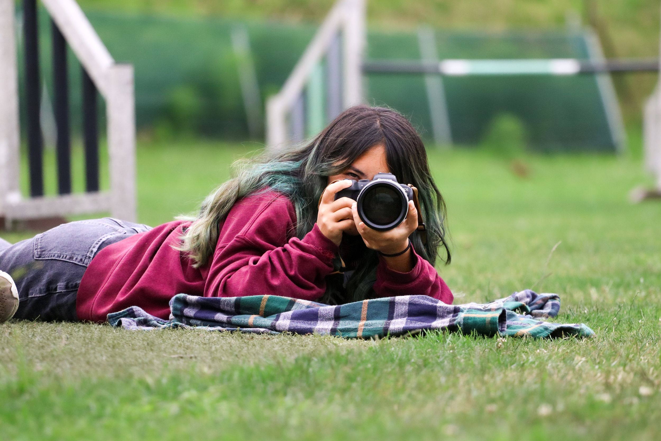 Photographer lying on grass with professional camera taking nature photos in outdoor setting.