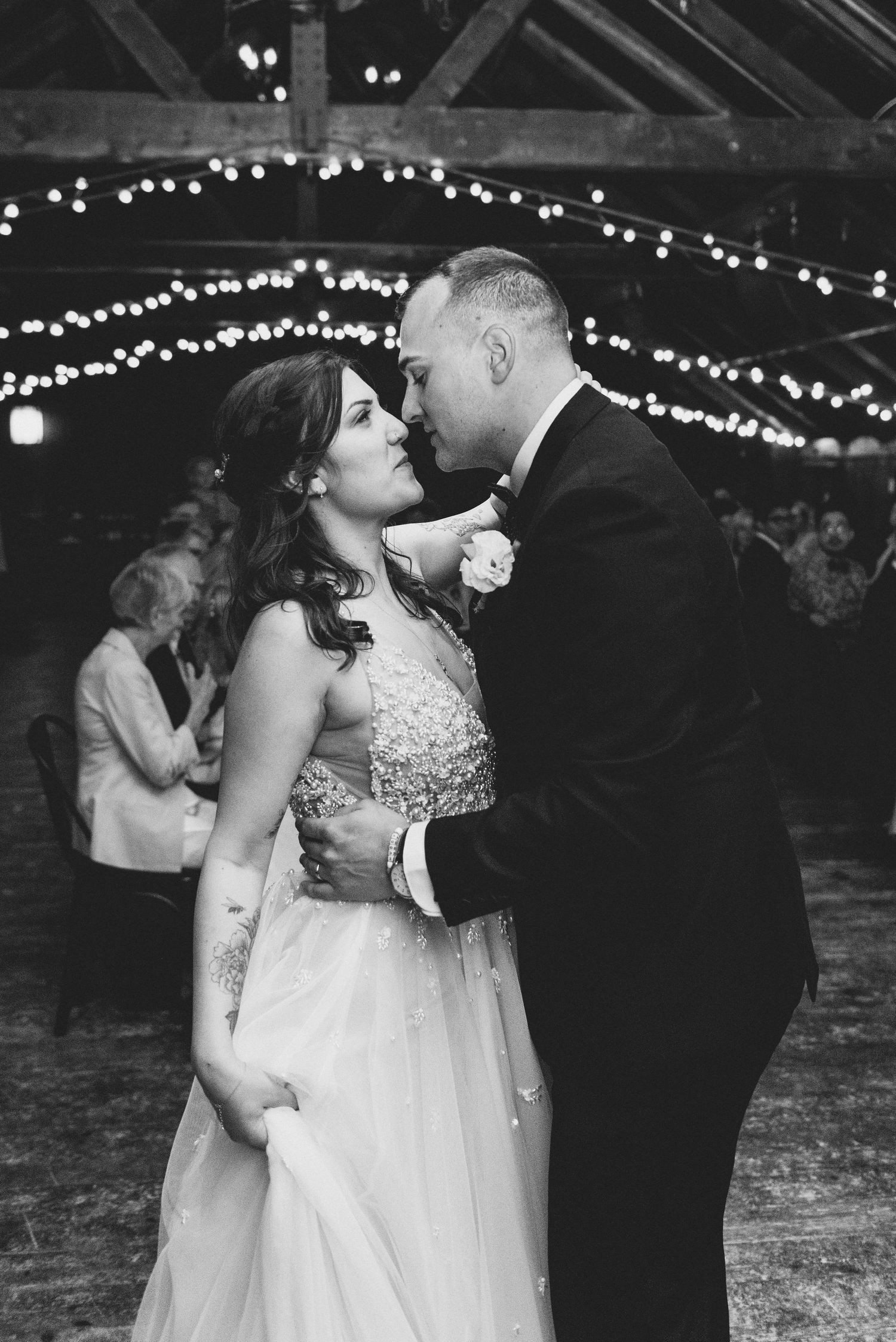 A tender black and white wedding moment with a couple sharing their first dance under glowing string lights.