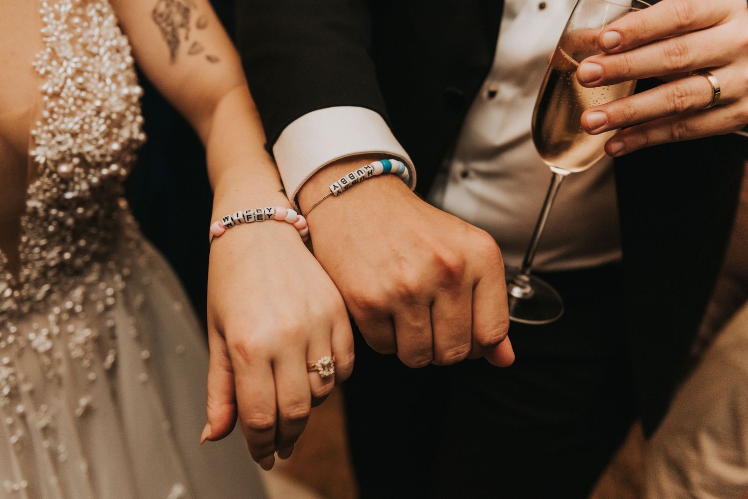 Close-up of newlyweds' hands showing wedding rings and sparkly bridal dress details.