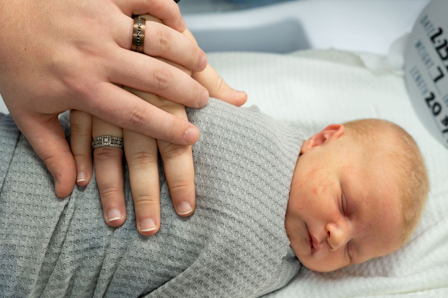 Caring hands rest on peaceful newborn swaddled in soft gray blanket.