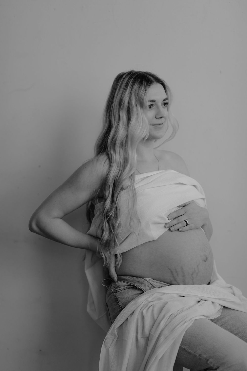 Black and white maternity photo with flowing fabric draping over pregnant belly in artistic style.