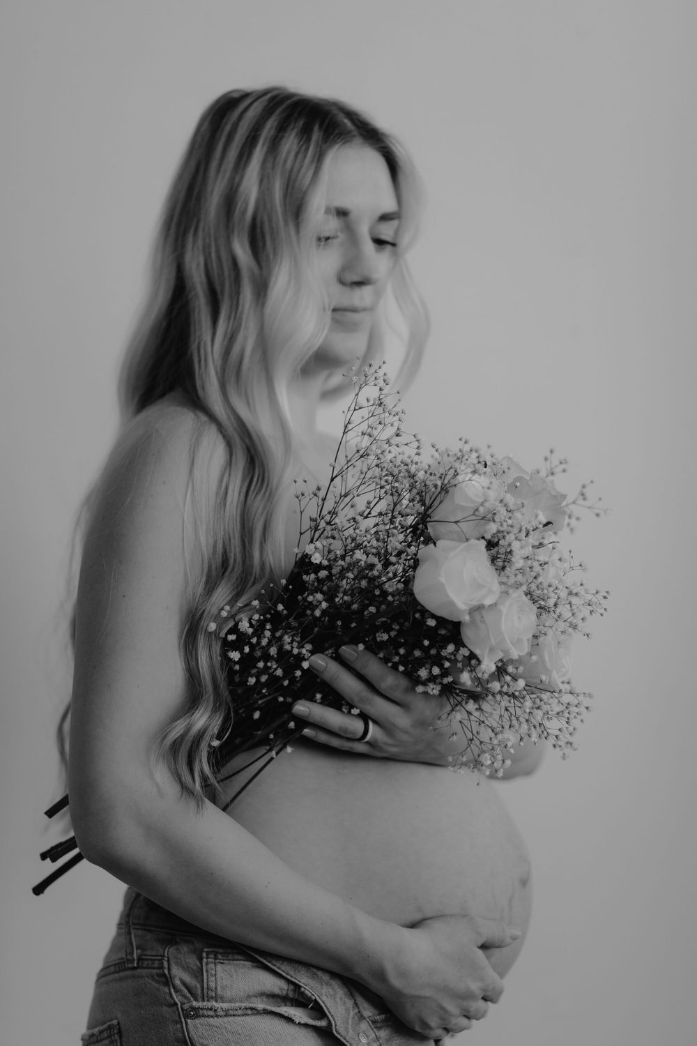 Black and white maternity photo featuring a side profile with baby's breath and roses bouquet held against the belly.