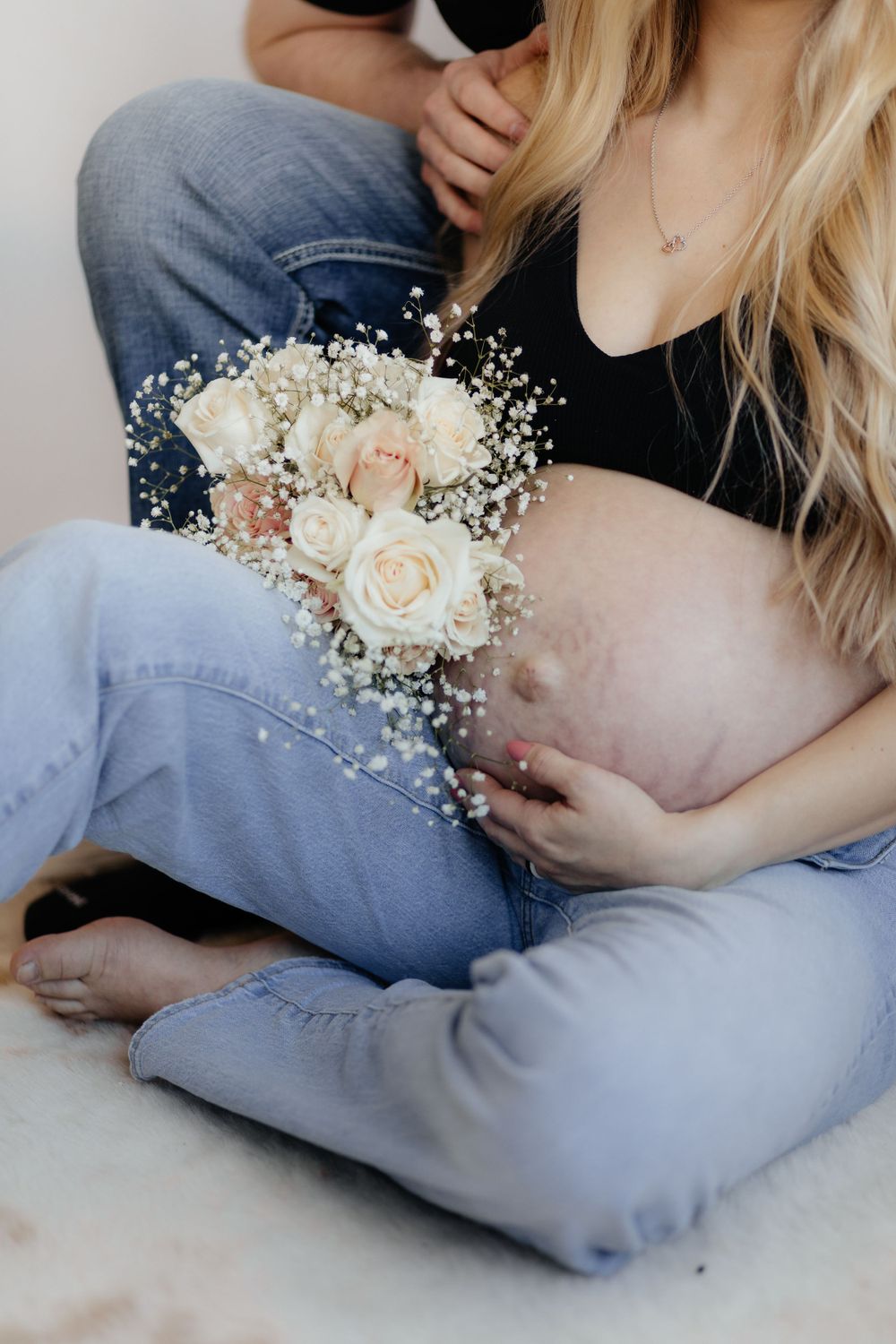 Close-up of maternity photo showing white roses and baby's breath bouquet resting on denim-clad lap.