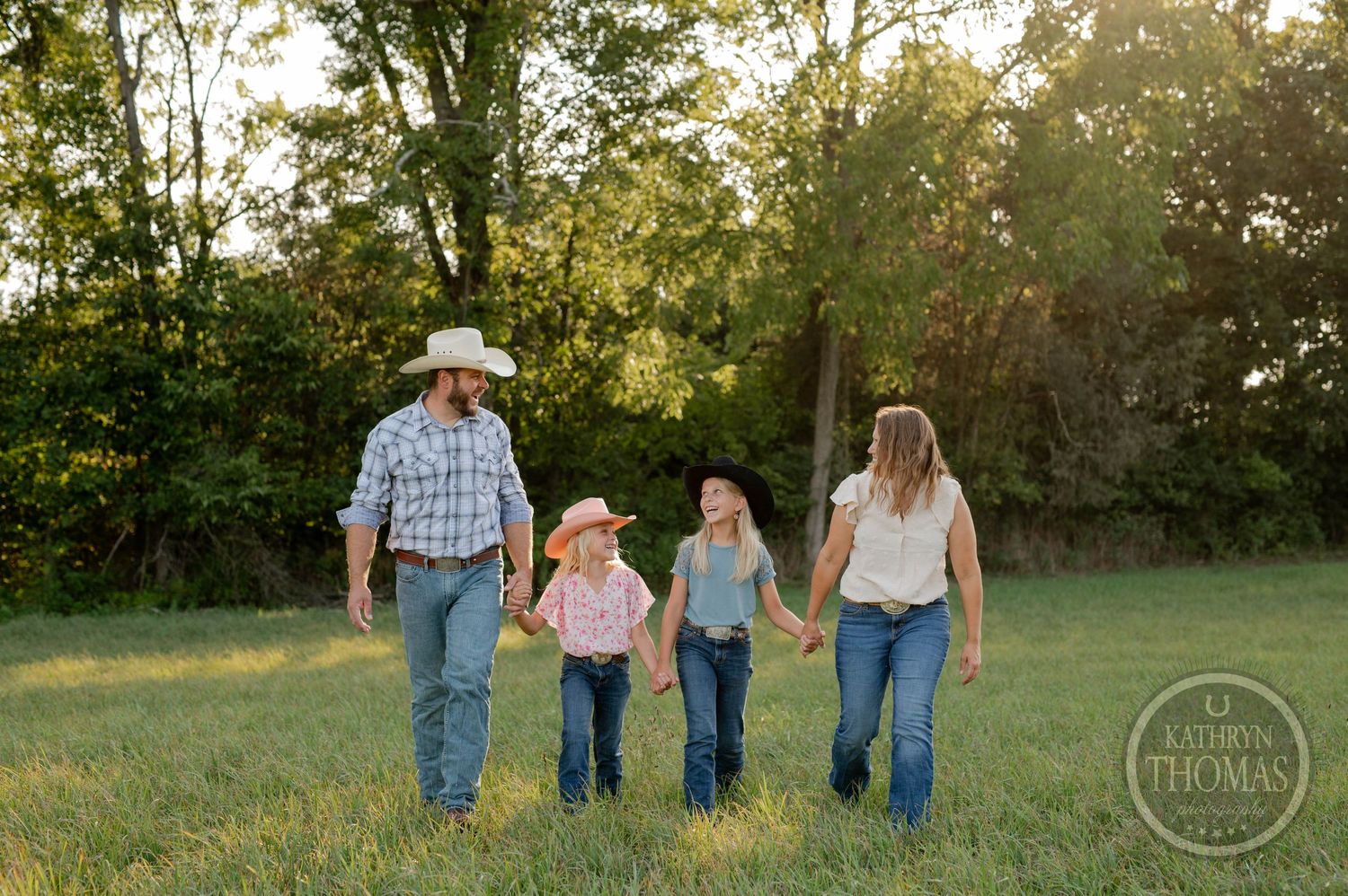 Family holds hands while walking through a grassy field at sunset.