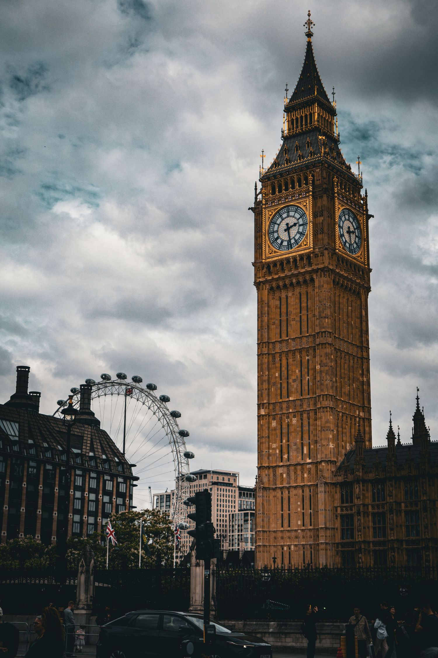 Big Ben tower and London Eye ferris wheel against a dramatic cloudy sky in Westminster.