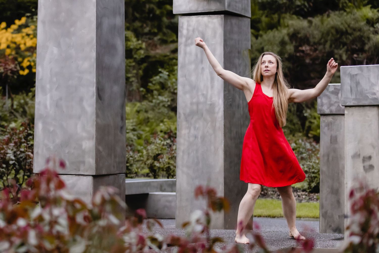 Someone in a flowing red dress dances gracefully among stone pillars and autumn foliage in an outdoor setting.