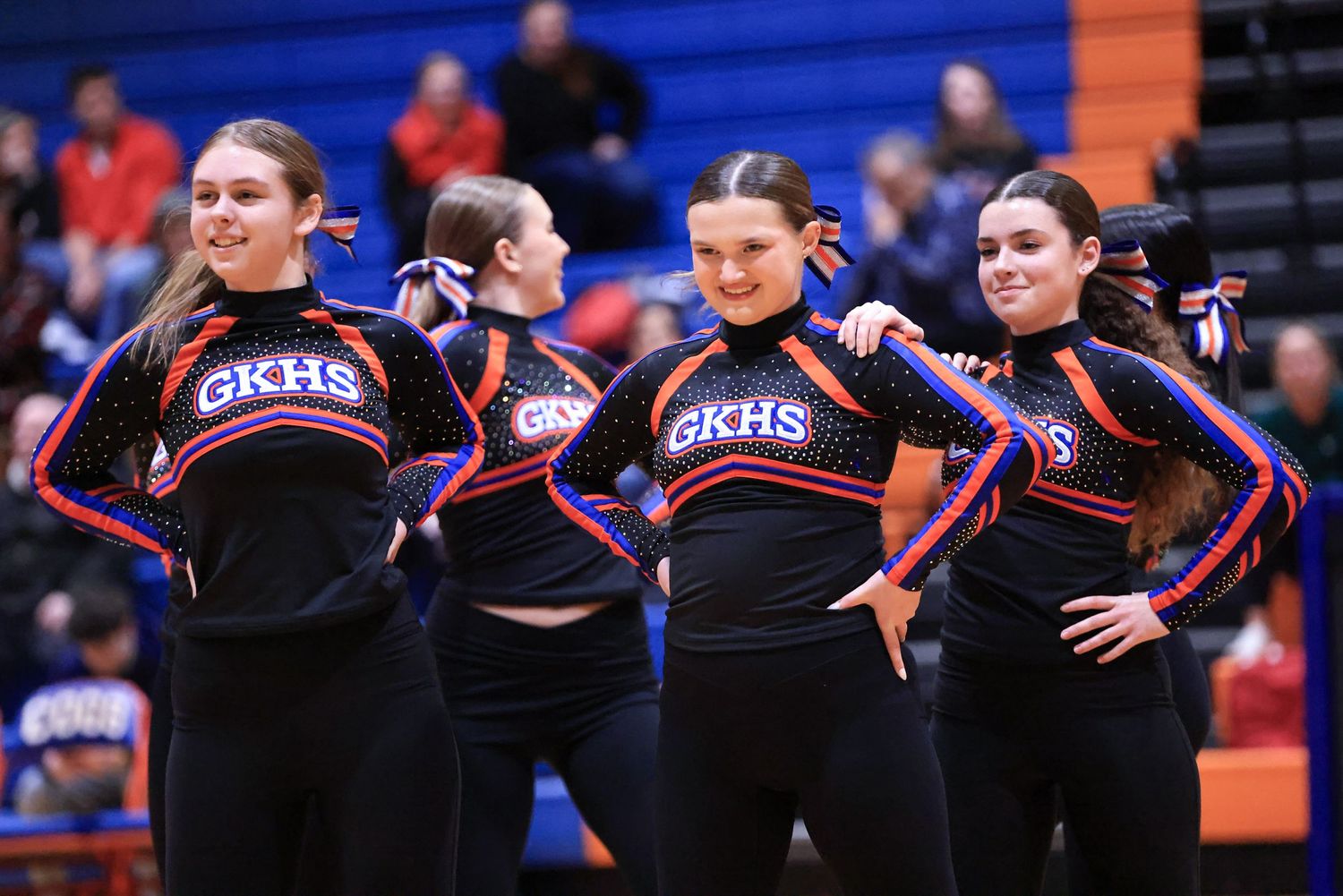Cheerleaders performing routine in black uniforms with blue and orange accents.