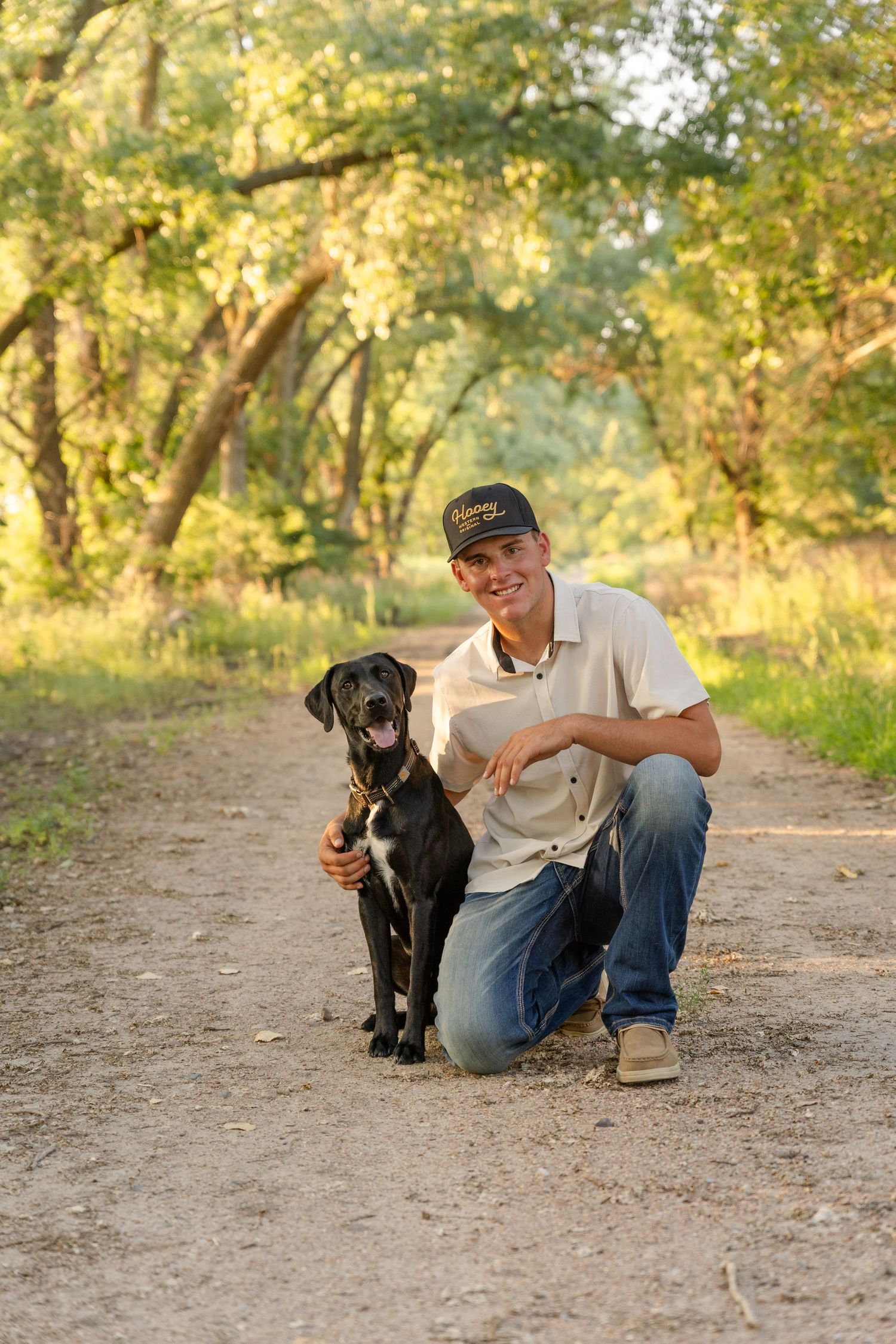 becky katzberg photography senior boy and his black lab hunting dog on a path with trees over the path at sunset