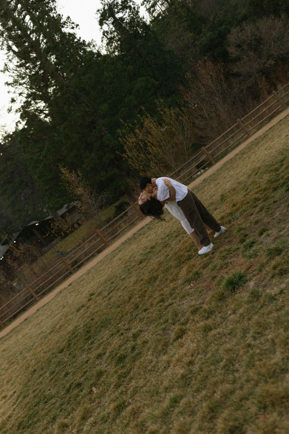 A couple in white outfits share a dramatic dip pose on a grassy hillside.