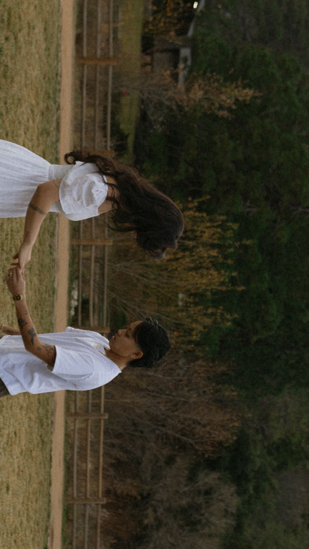 A couple in white outfits dance together in a rustic outdoor setting during golden hour.