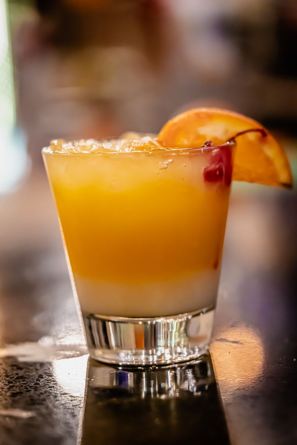 Orange cocktail garnished with citrus slice and cherry served in a rocks glass with ice.