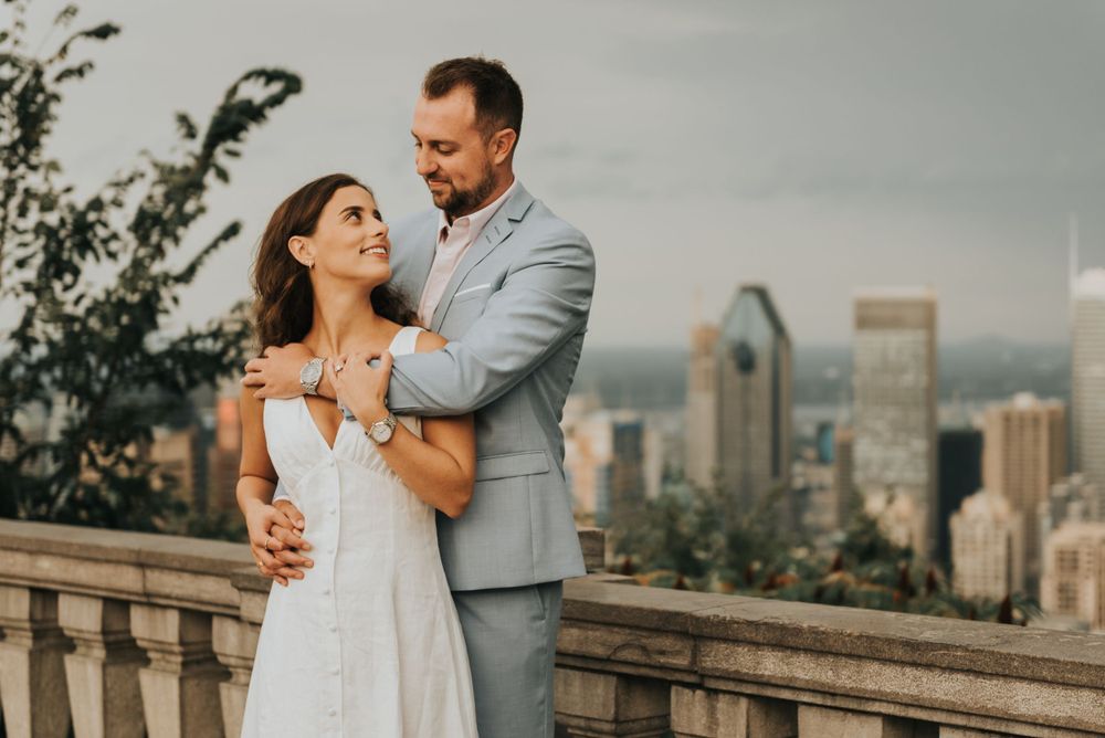 Romantic wedding couple embracing on balcony overlooking Montreal cityscape at sunset.