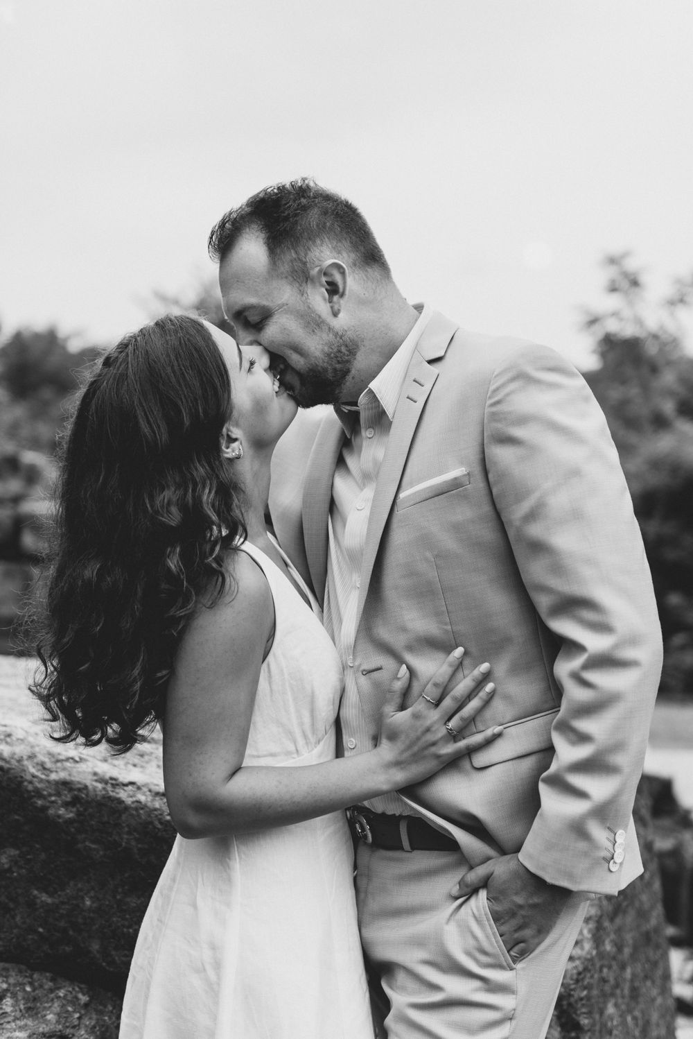 A black and white portrait of a couple in intimate embrace outdoors in formal wear.