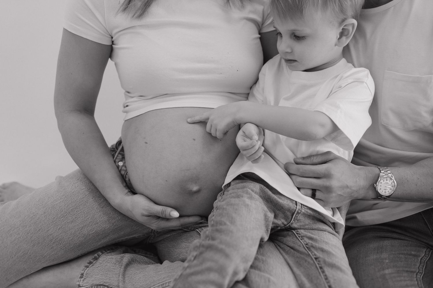 Two people embrace against a white wall in a romantic maternity photo capturing a tender moment during pregnancy.