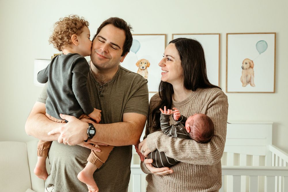 A warm family moment at home with a toddler and newborn baby next to framed nursery wall art.