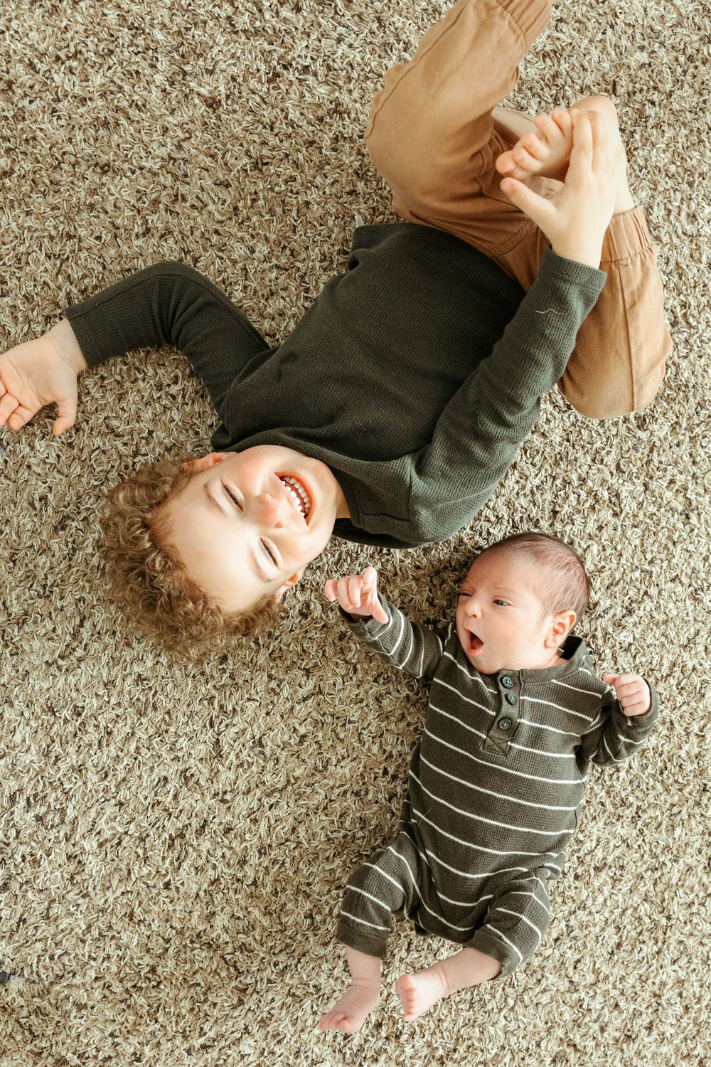 Two people lying on a gray carpet together, one wearing a dark sweater and one in striped clothing.