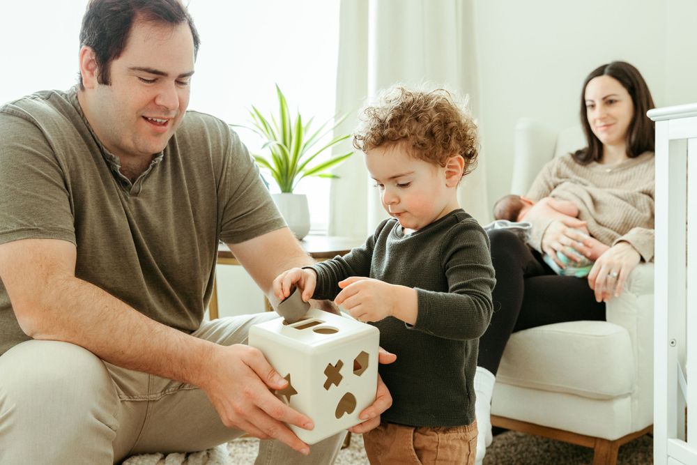 Family spending quality time together in living room with child opening gift box while mother sits on couch.