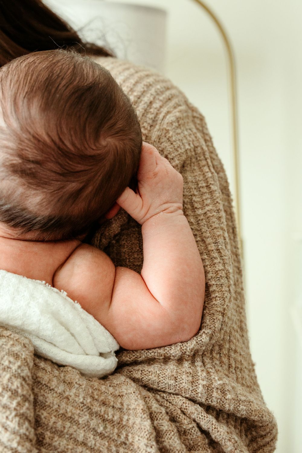 Baby wrapped in cozy brown knit blanket sleeps peacefully against soft white bedding.