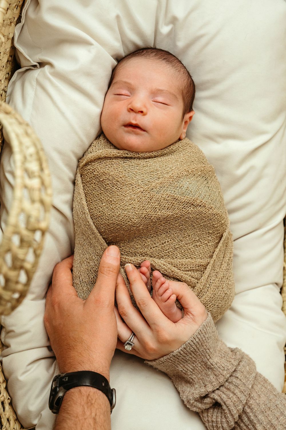 A sleeping newborn baby swaddled in a soft brown blanket resting peacefully on white fabric.