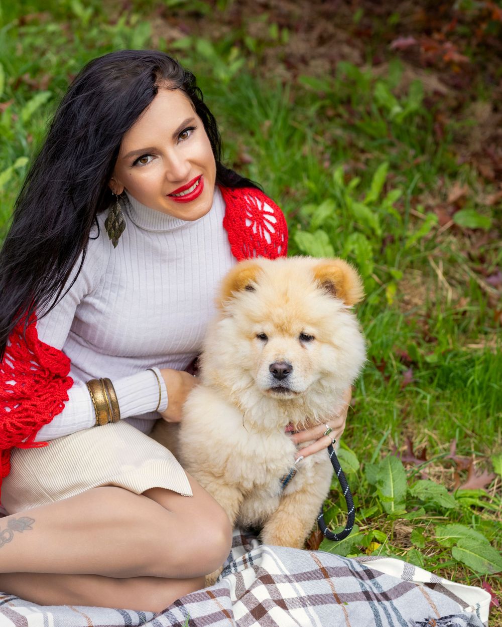 Woman in white sweater and red cardigan hugging fluffy cream-colored Chow Chow dog outdoors.