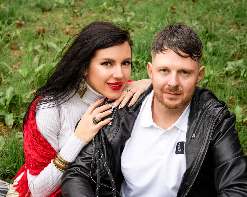 Couple sitting together outdoors with woman in red cardigan and man in leather jacket.