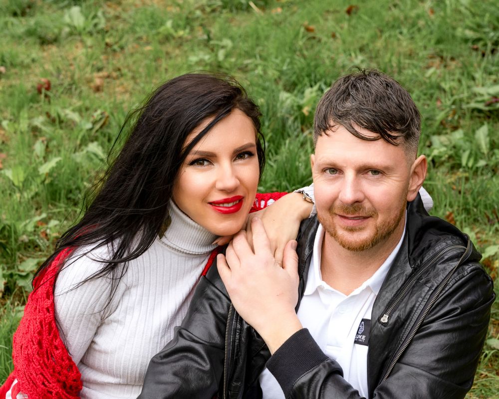 Couple smiling together outdoors with woman in red cardigan and white turtleneck.