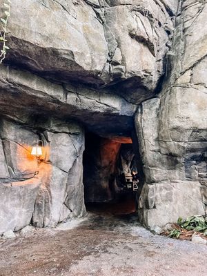 Illuminated rock tunnel entrance with rugged stone walls and dim lighting leads into a mysterious cave system.