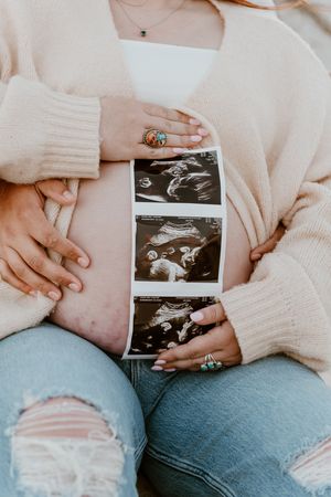 A series of maternity photos showing someone holding ultrasound images while wearing a cream sweater and distressed jeans.