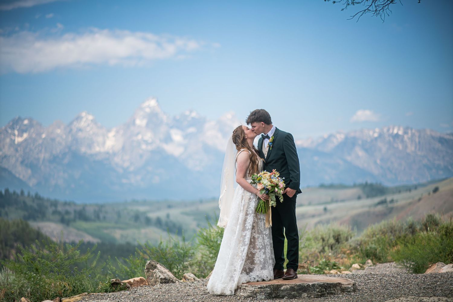 A couple in wedding attire share an intimate moment outside a majestic white church under dramatic cloudy skies.