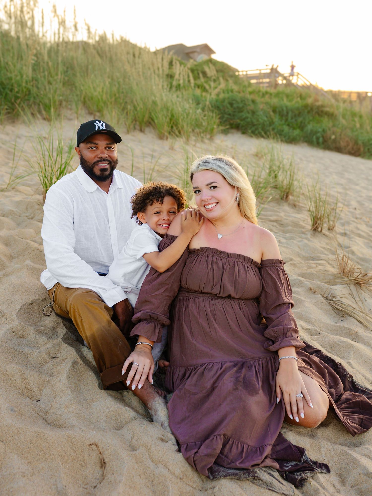 Family relaxing together on sandy beach dunes during golden hour.