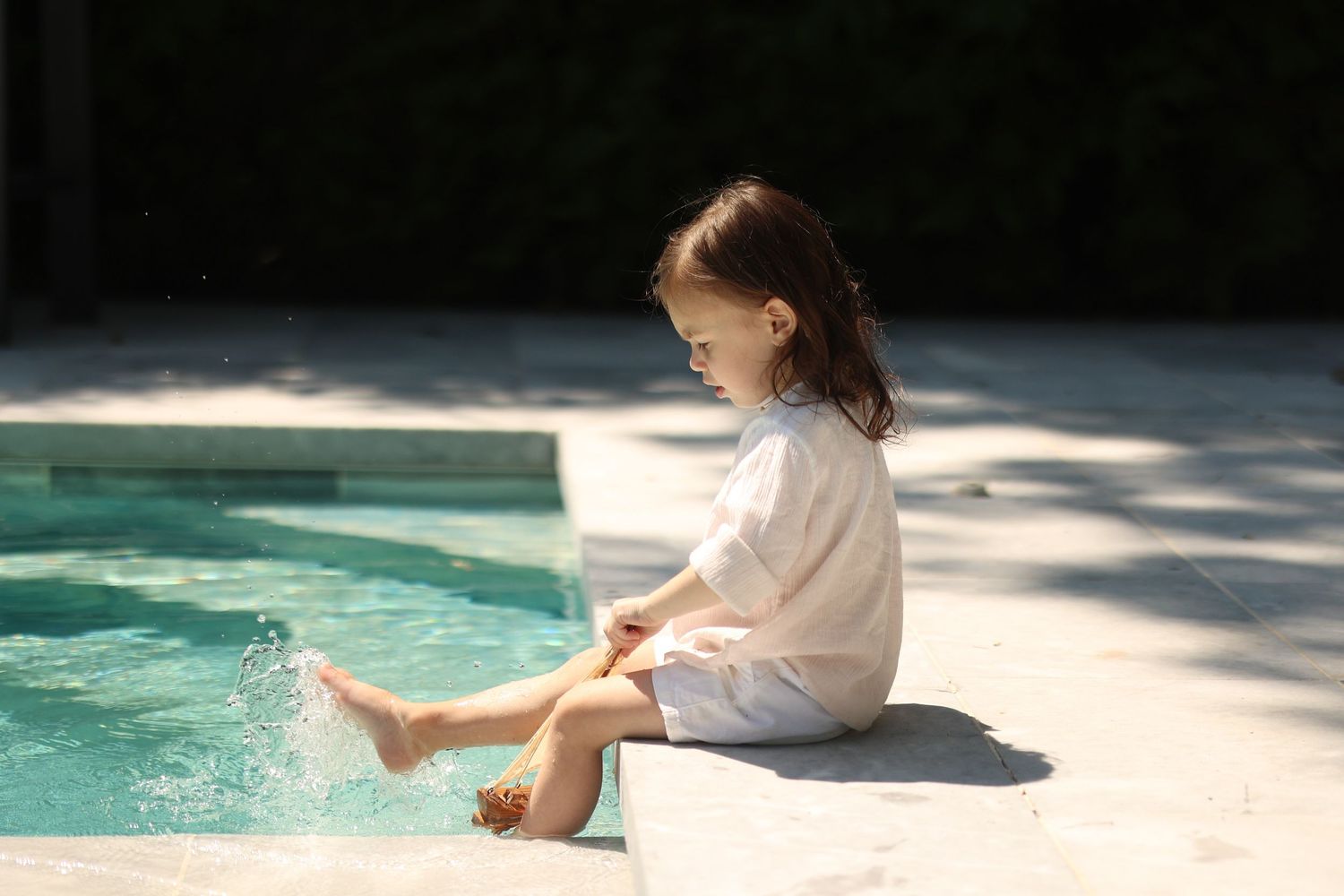 Upsherin boy sitting in the sunshine splashing his foot in the clear water of serene pool