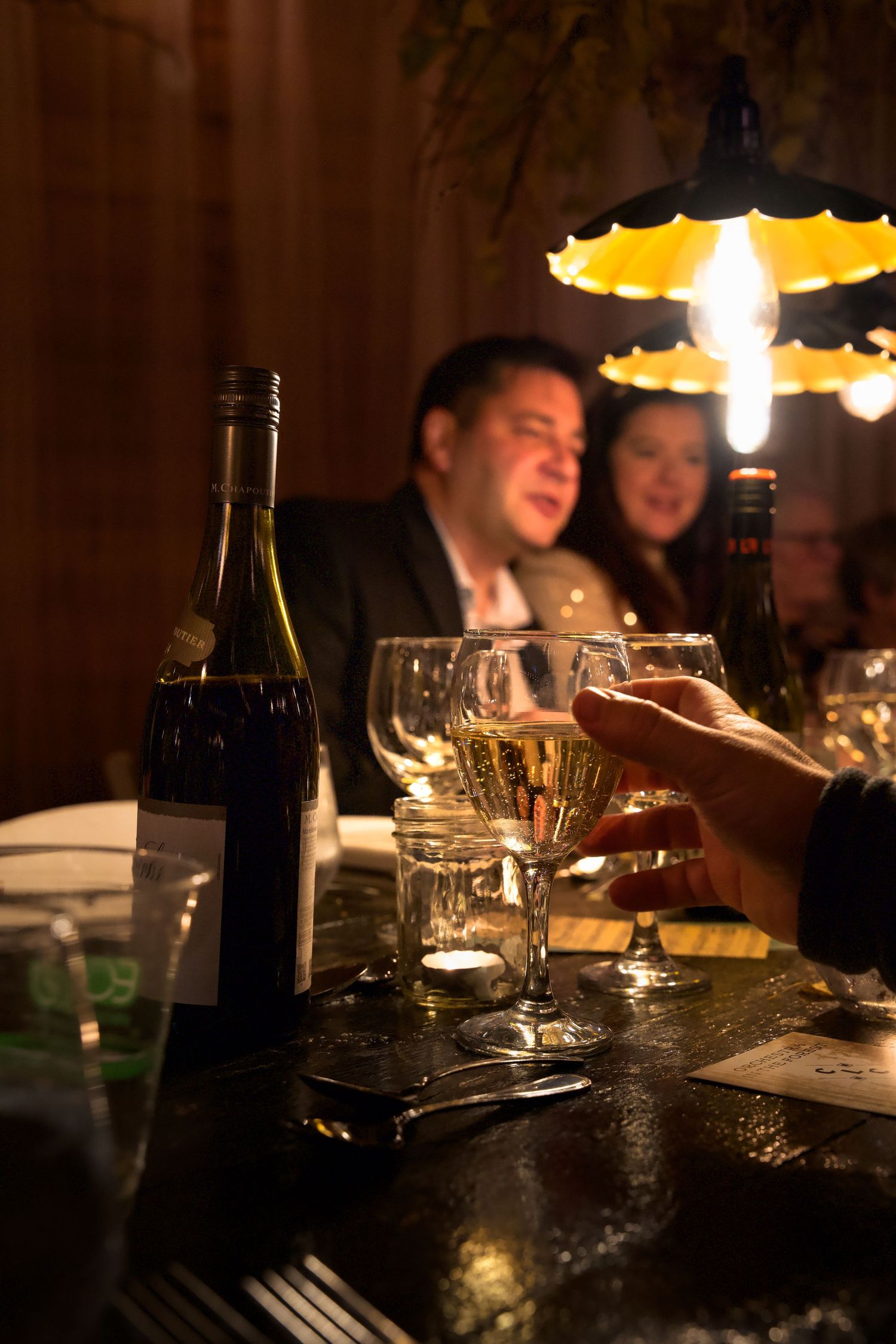 Wine bottles and glasses on a dark table create an intimate dining atmosphere.