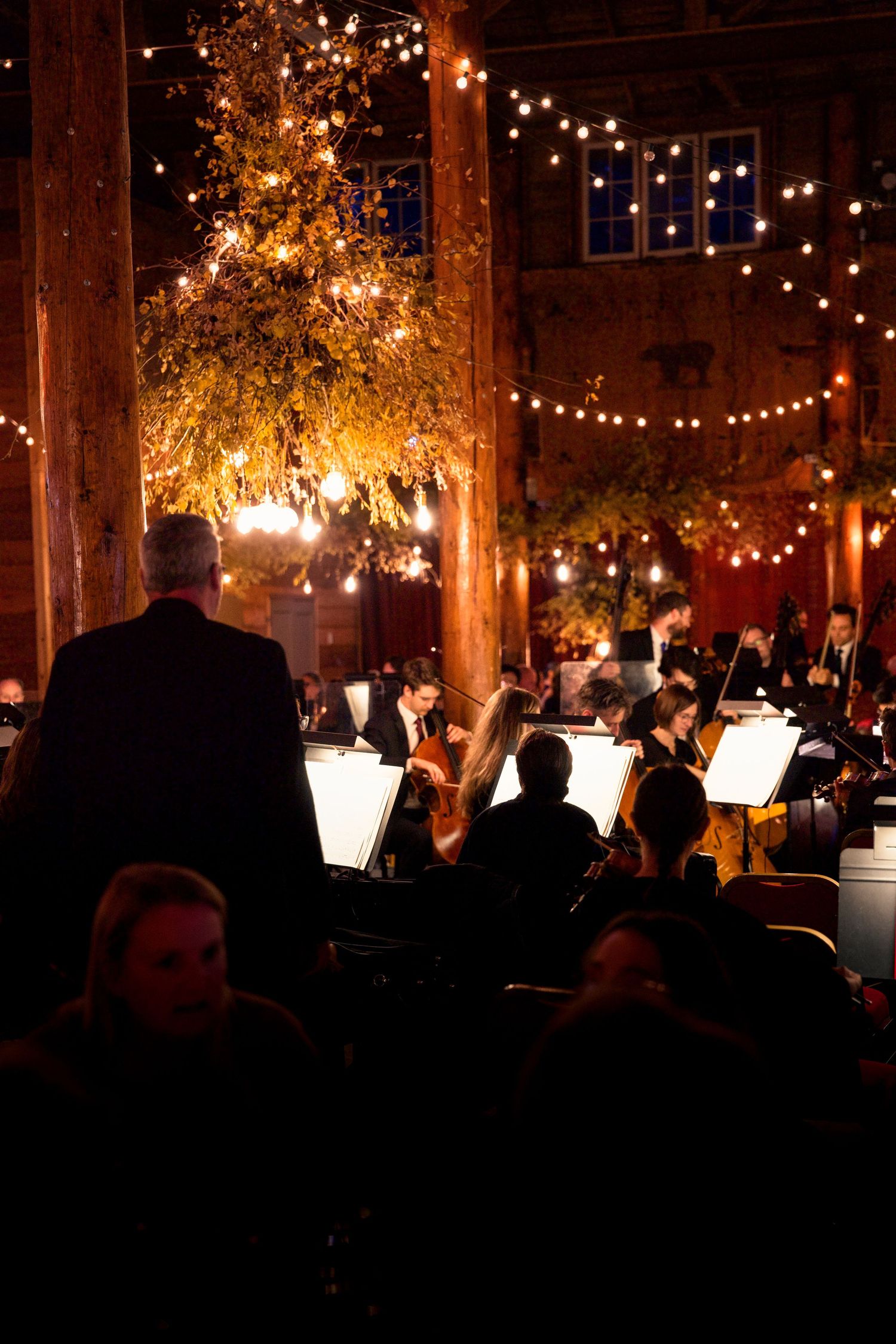 Orchestra performing in a warmly lit venue with string lights and autumn decor.