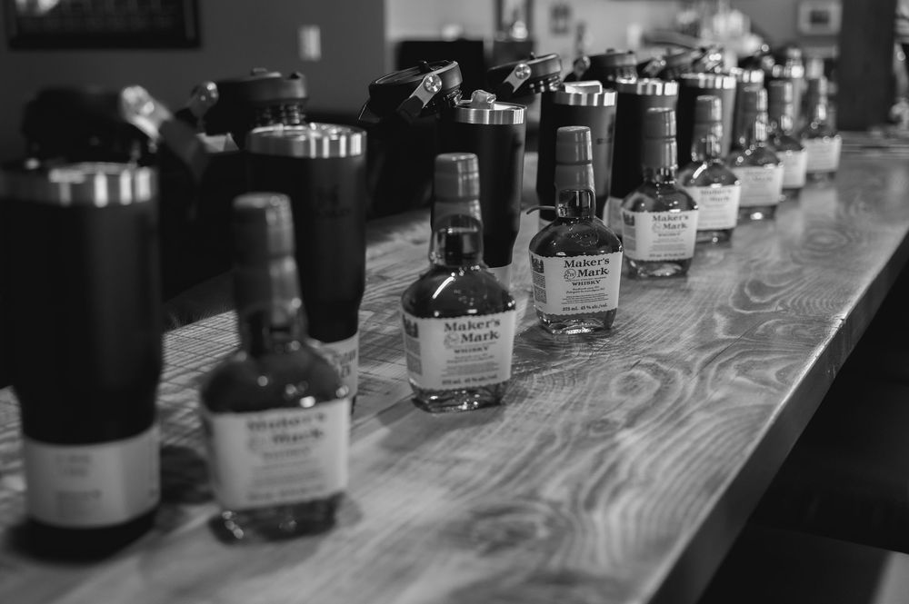 Row of whiskey bottles lined up on wooden bar surface at wedding reception.