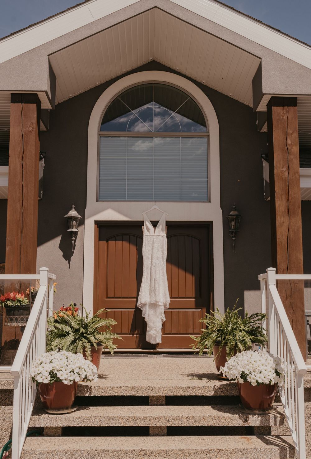 Wedding dress hanging outside rustic venue entrance with wooden accents and arched windows.