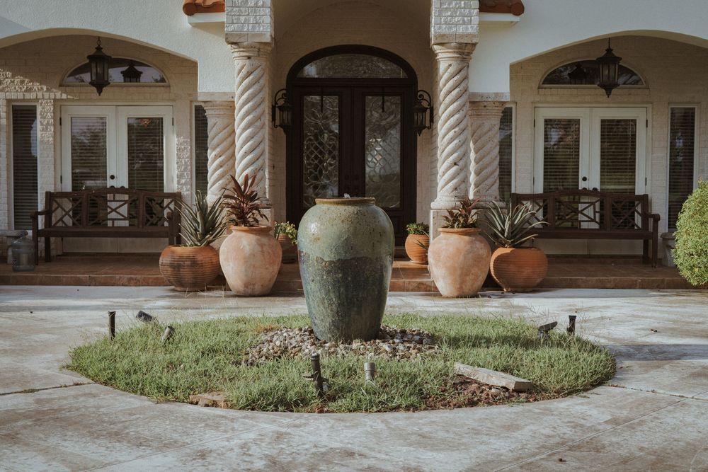 Mediterranean style entrance with stone columns and large decorative pottery around circular fountain.