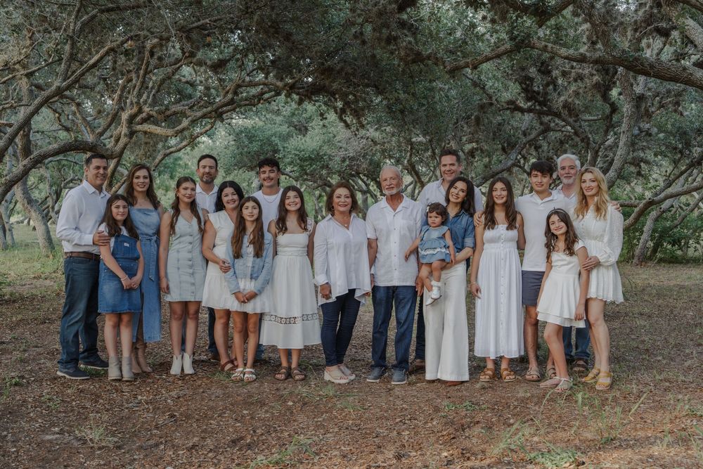 Extended family gathering in a wooded outdoor setting wearing coordinated white and blue outfits.