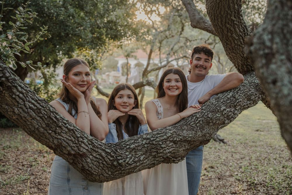 Family members posing playfully on a curved tree branch in a rustic outdoor setting.