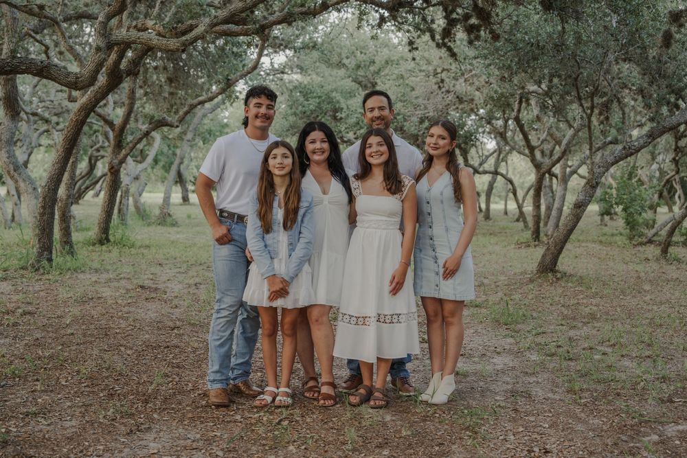 Casual outdoor family photoshoot with people arranged among oak trees.