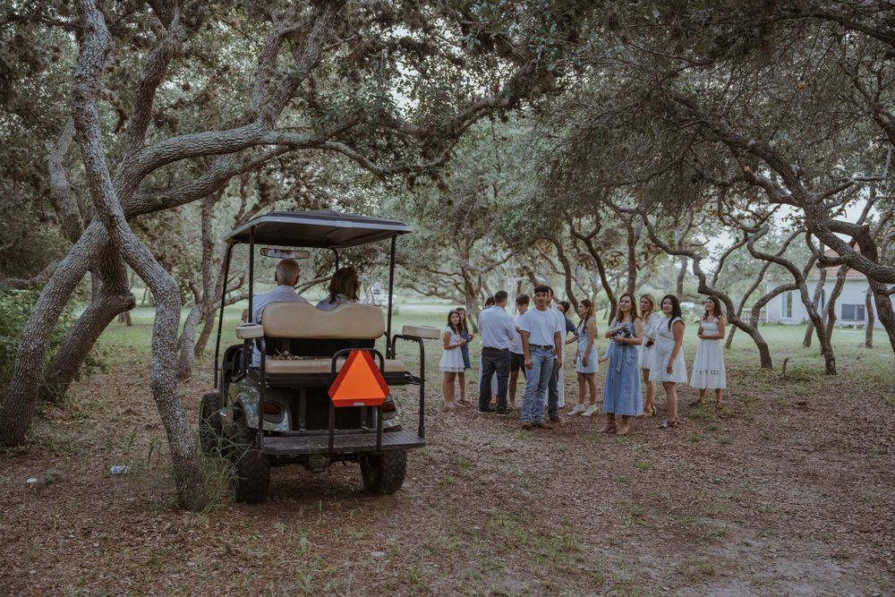 Family gathering in a wooded area with vintage truck visible in background.