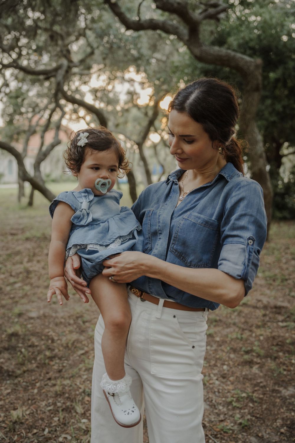 Mother and child in coordinated denim outfits playing together in a wooded setting.