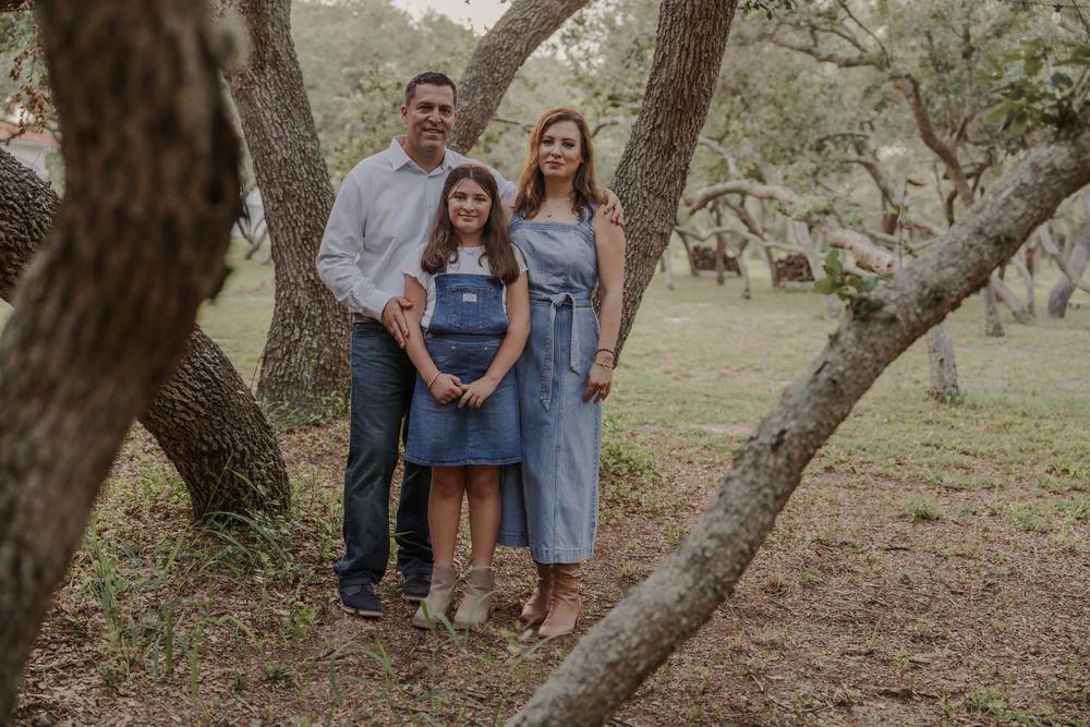 Family members posing casually around a curved tree trunk in natural lighting.