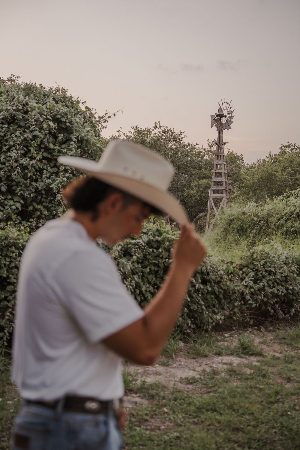 Silhouette of person in cowboy hat with windmill in rural background at sunset.