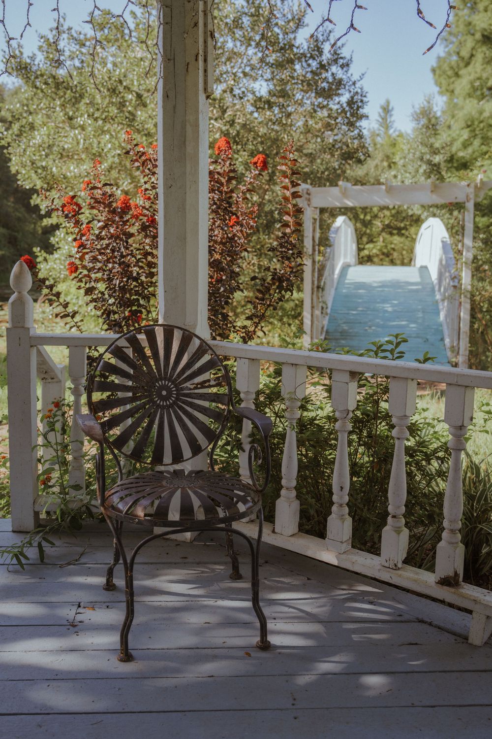Rustic porch with decorative spinning wheel silhouettes and red flowers against white railing.
