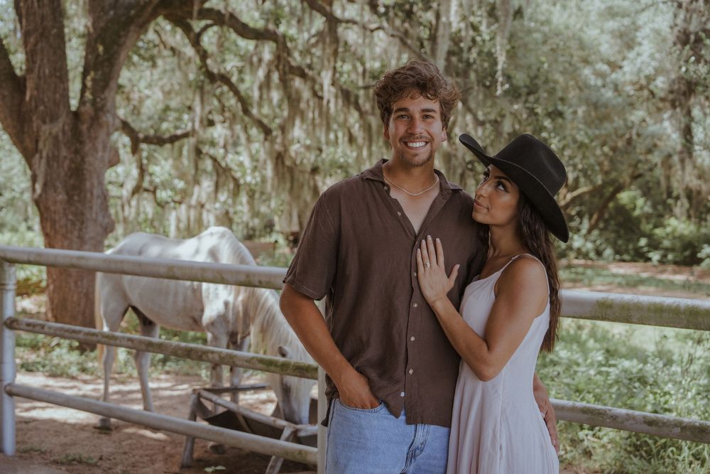 Romantic couple sharing intimate moments by a rustic wooden fence under oak trees.