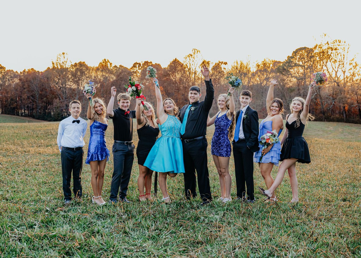 Large group poses together in semi formal attire on grassy field during sunset.