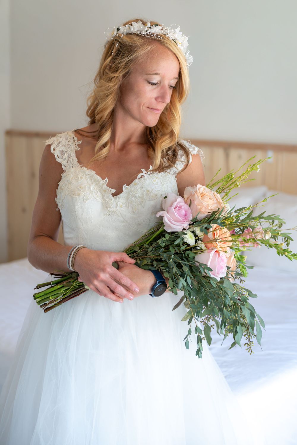 A person in a white lace wedding dress sits gracefully with a pastel pink and green floral bouquet.