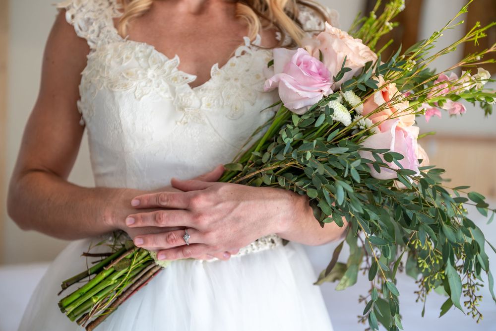 A close-up view of a bride holding her bridal bouquet featuring pink roses, greenery and delicate white lace details.